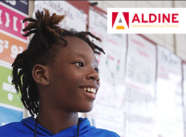 A smiling middle school student at Aldine Independent School District standing in front of board covered with math posters and papers