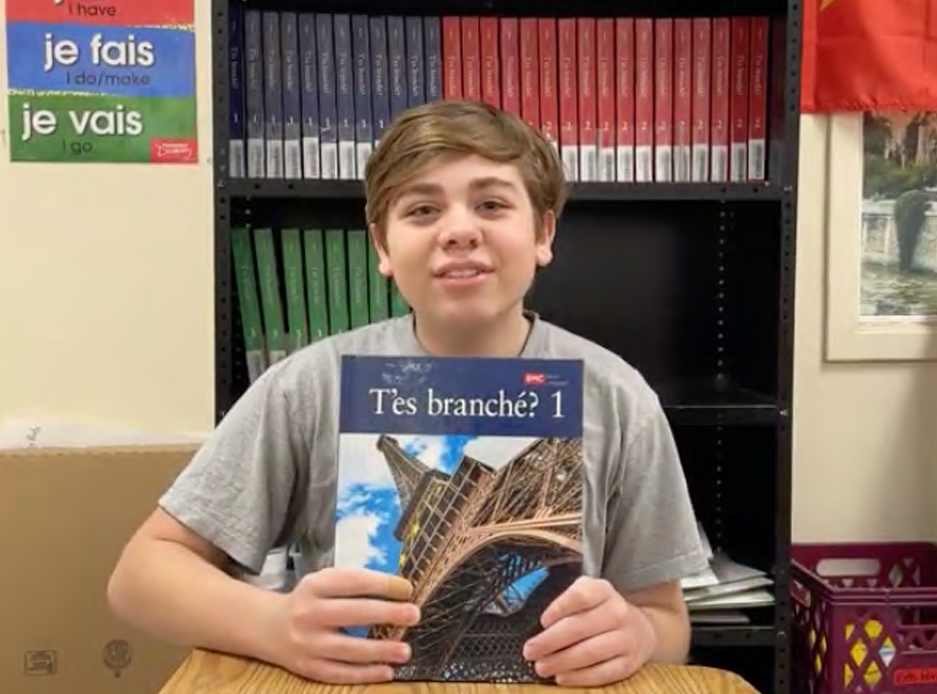 Student from Colombus, OH sitting in a desk showing a copy of a T'es Branché? student book. 